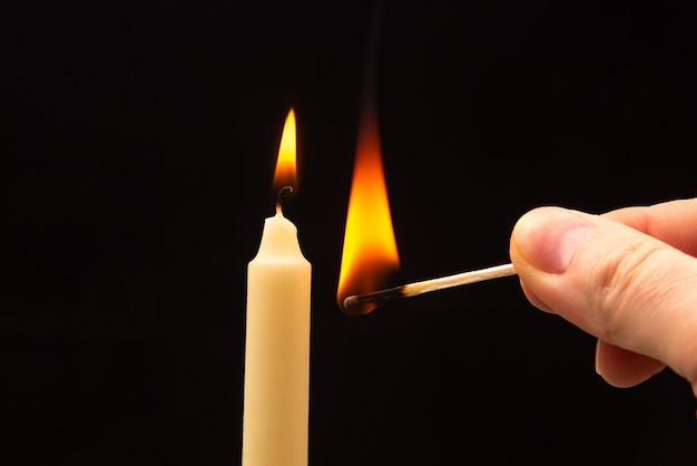 Lighting a candle with a wooden match on a dark background Burning candle fire