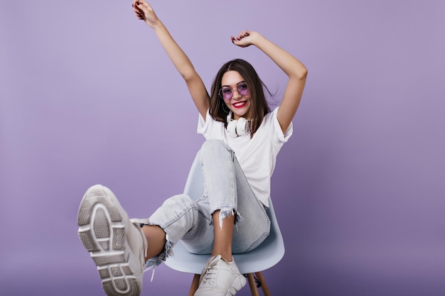 Lightlytanned girl with bright makeup expressing positive emotions on purple background Studio photo of amazing young lady fooling around during photoshoot