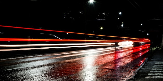 夜の車のライト。街灯。夜の街。長時間露光写真の夜道。道路上の色付きの光の帯。雨上がりの濡れた道路。