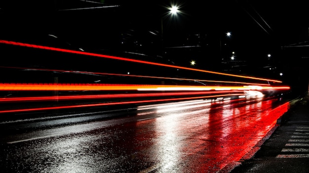 夜の車のライト。街灯。夜の街。長時間露光写真の夜道。道路上の色付きの光の帯。雨上がりの濡れた道路。