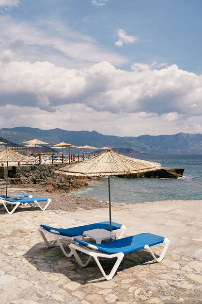 Ligstoelen met tafel staan onder een parasol op een geplaveid strand