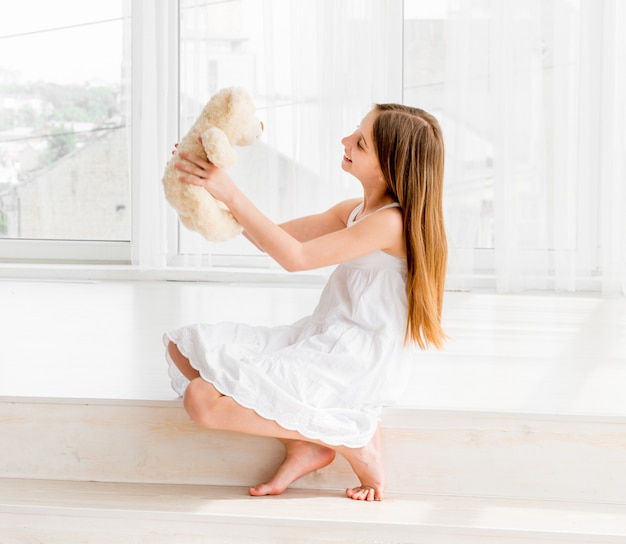 Liittle girl sitting on the floor and holding Teddy bear toy