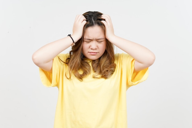 Lijdend aan hoofdpijn van mooie Aziatische vrouw die geel TShirt draagt dat op witte achtergrond wordt geïsoleerd