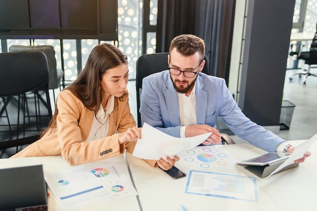 Likable purposeful business partners carefully studying financial documents with charts at the boardroom table at the meeting room.