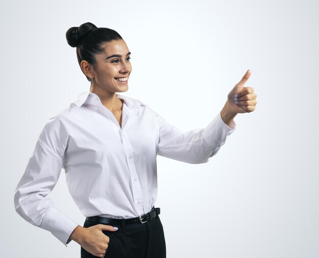 Foto come il concetto con la giovane donna felice in camicia bianca che tiene i pollici su su sfondo chiaro vicino isolato