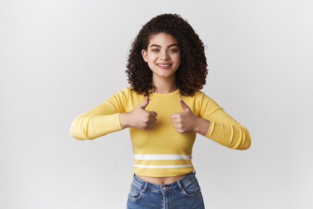 Like follow share Attractive satisfied confident sassy young girl curlyhaired approve cool project friend present show thumbs up support coworker idea agree recommend friend buy outfit shopping