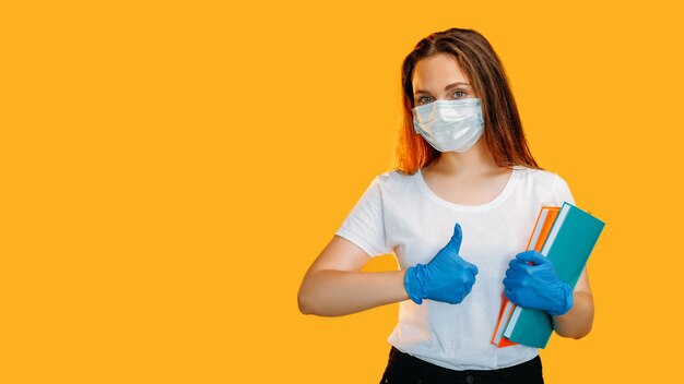 Like gesture socially distanced confident female teacher in protective face mask gloves with books