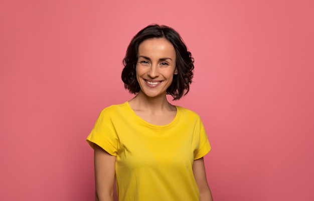 Like a sunshine. Portrait of a cheerful young woman with short dark hair in a yellow t-shirt, who is looking in the camera and smiling.