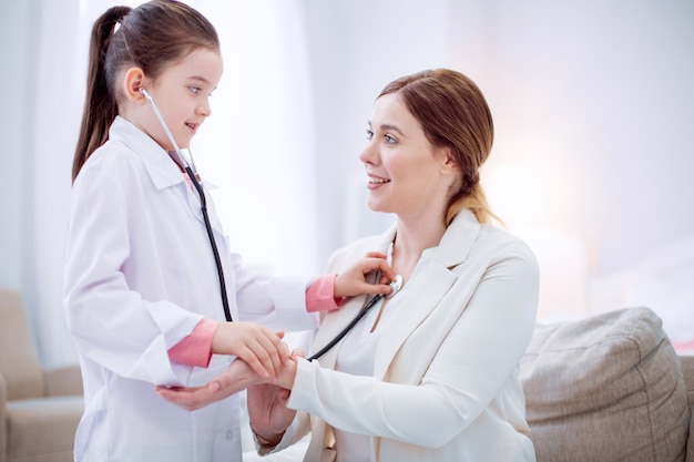 Like this. Glad optimistic girl learning how to use stethoscope while playing with female doctor