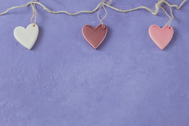 on a lilac background, three ceramic hearts (white, pink and purple) are hung on a rope 