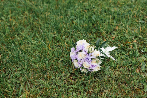 На зеленой траве лежит сиреневый и бежевый свадебный букет.