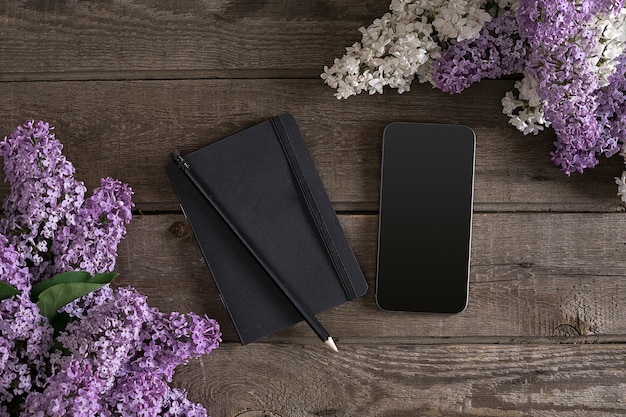 Lilac blossom on rustic wooden background with notebook for greeting message. Top view. Mother's Day. Spring background concept.