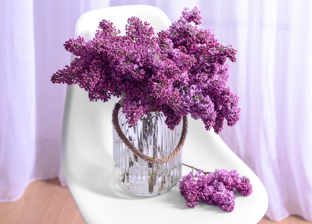 Lilac bouquet in glass jar on white stool