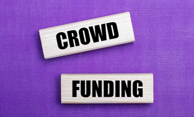 On a lilac bright surface, light wooden blocks with the text CROWD FUNDING