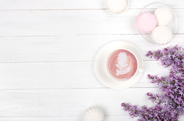 Lilac, coffee with latte art and marshmallow on white wooden table. Romantic morning. Flat lay