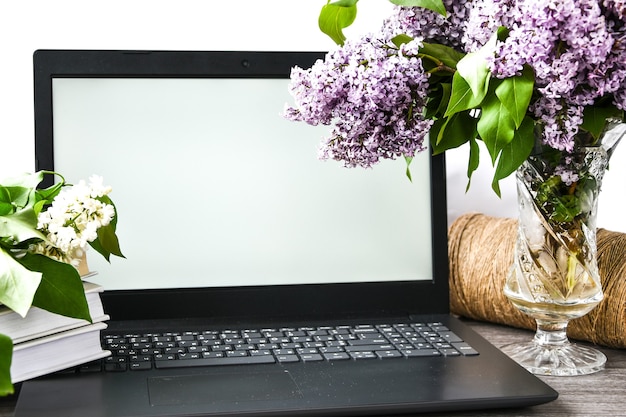 Lilac flower bouquet in glass vase with open laptop white screen and books