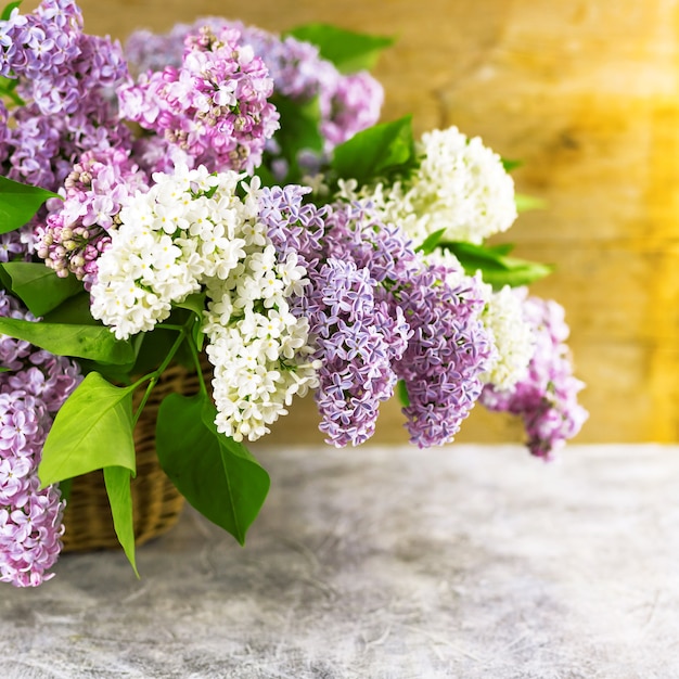 自然な木製の壁の近くのコンクリートのテーブルの枝編み細工品バスケットのライラックの花の枝