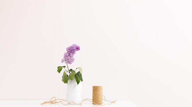 Lilac flowers in a vase with twine and mirror on a white table with blank copy space