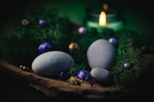 Lilac golden stone lies in the bark of a tree with green moss gray stones and a burning candle on a green