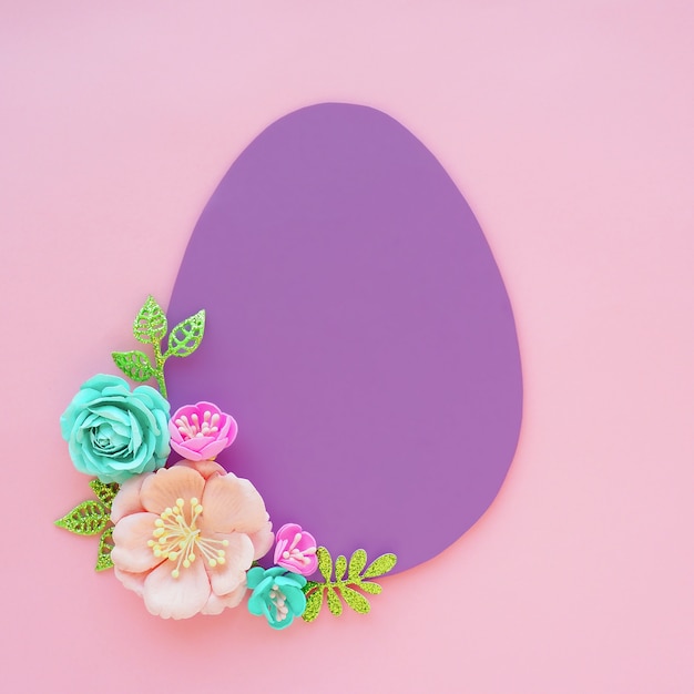 Lilac paper egg on a pink background and paper artificial flowers and leaves. Space for text. Easter concept.
