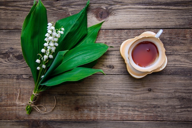 Lily of the valley bouquet and a cup of tea on a wooden surface