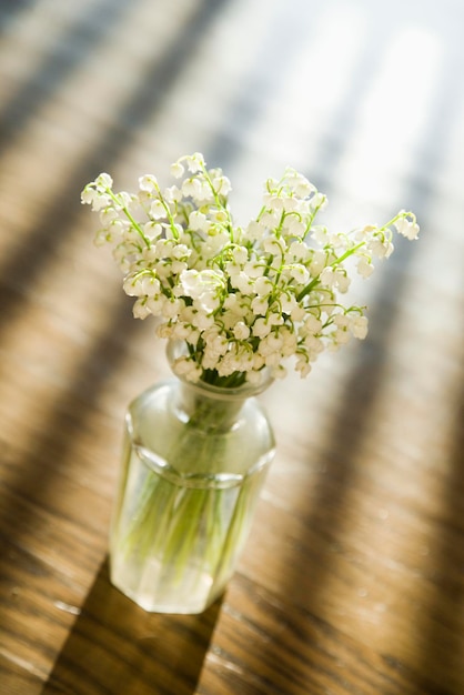 Lily of the valley flowers in glass vase on wooden table