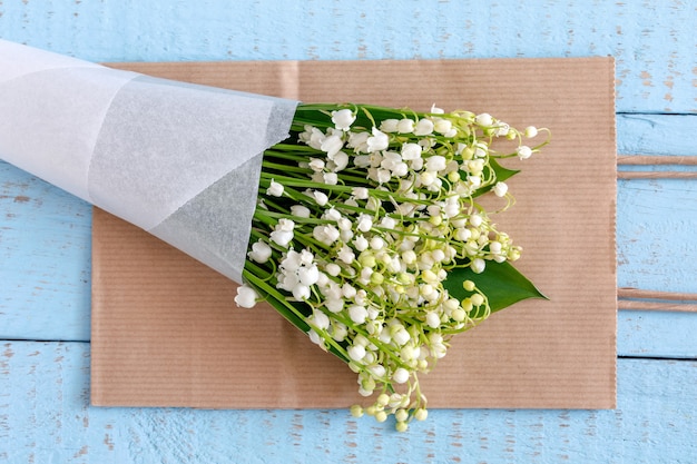 Lily of the valley flowers in a paper bag on blue.