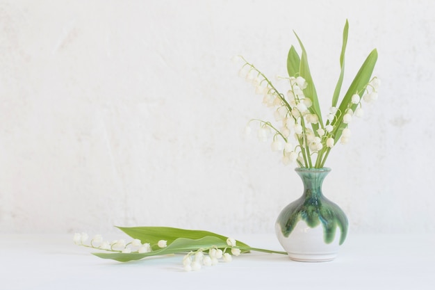 Lily of the valley in little vase on surface old white wall