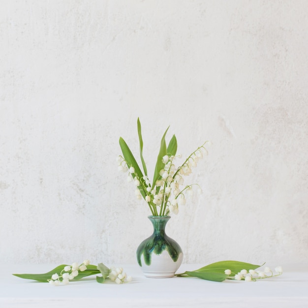 Lily of the valley in little vase on surface old white wall