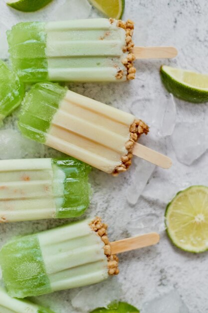 Lime and cream homemade popsicles or ice creams placed with ice cubes on gray stone backdrop Flat lay top view