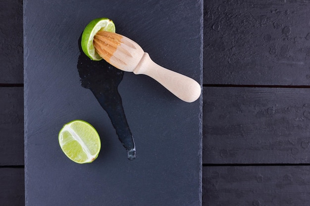 Lime halves en houten juicer op leisteen bord Lime op donkere achtergrond Verse limoensap stroomt