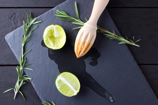 Lime halves and wooden juicer on slate board Lime and rosemary on black background Fresh lime juice