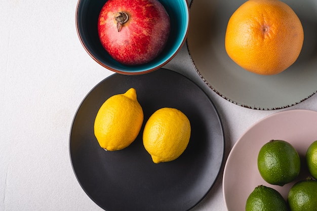 Lime, lemon, grapefruit and pomegranate in colorful plates on white