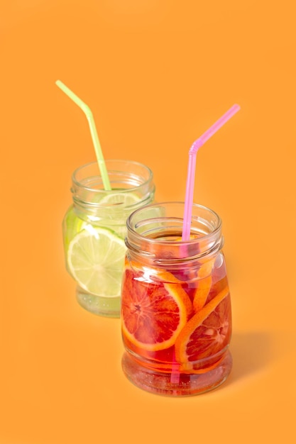 Lime and red orange lemonade in glass jars on orange background