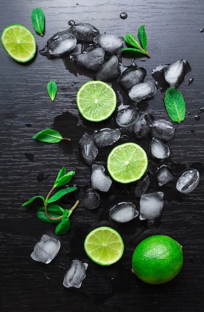 Limette, foglie di menta e cubetti di ghiaccio sul nero. ingredienti per il cocktail mojito