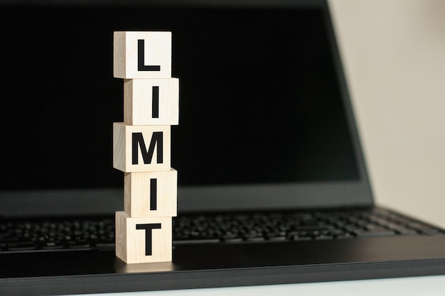 Photo limit word made with building blocks on the black keyboard. a row of wooden cubes with a word written in black font is located on a black keyboard.