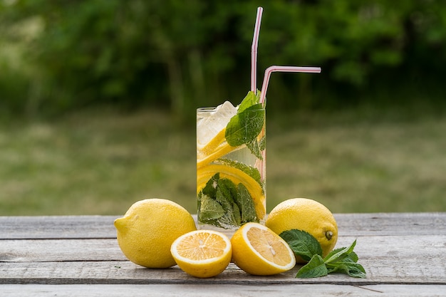 Limonade met citroen, munt en ijs, in een glas, over oude houten tafel