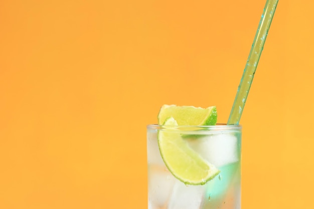 Limonade met ijs en limoen op een feloranje achtergrond Ruimte kopiëren Drankje met een rietje close-up