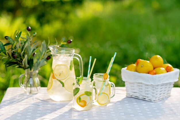 Limonade verfrissend drankje in een kruik en potten met citroenen, verse munt en ijs met een mand met citroenen en kumquat op een tuintafel. Zomer buiten picknick. Zachte selectieve focus.