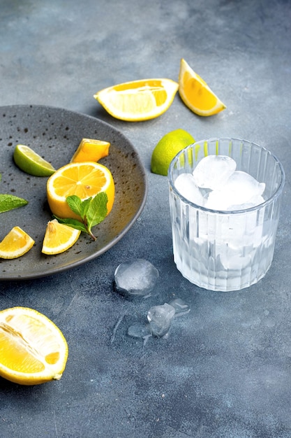 Foto limonade voorbereiding glas met ijsblokjes verse ingrediënten citroen en munt op grijze keramische plaat