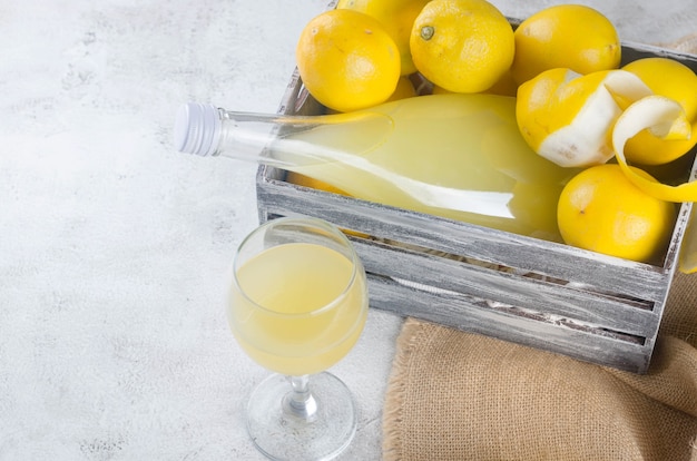 Limoncello in glass bottle and fresh ripe yellow lemons on the grey background, traditional homemade sweet Italian lemon liqueur, strong alcoholic drink and fresh ripe yellow lemons.