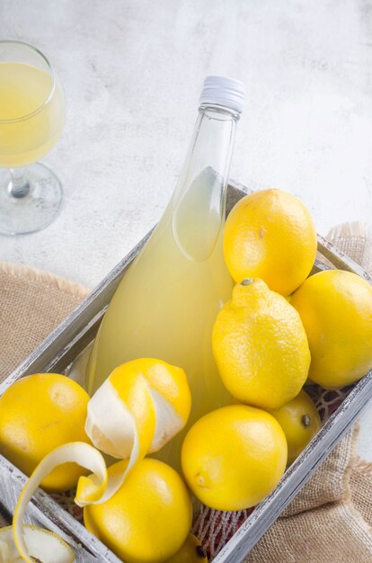 Limoncello in bottiglia di vetro e limoni gialli maturi freschi sullo sfondo grigio, tradizionale