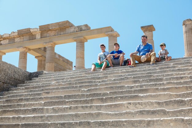 リンドスロードス島ギリシャ2015年9月3日リンドスロードスギリシャの古代アクロポリスのグランドヘレニスティックポルティコの列柱の近くの階段で休んでいる観光客