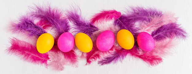 Photo line of pink and yellow bright easter eggs boiled and painted with feathers on white wooden table