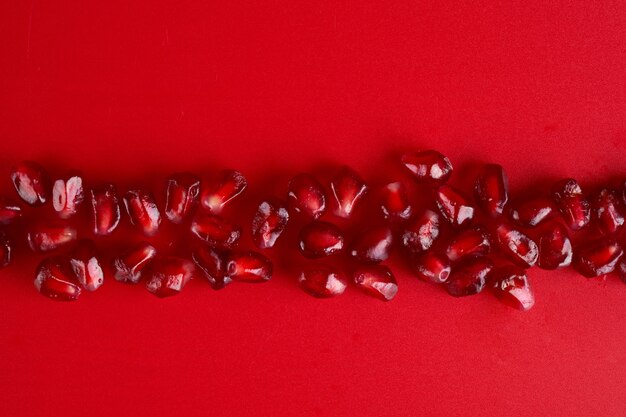 Line of ruby ripe fresh juicy pomegranate seeds close up isolated on red background with copy space