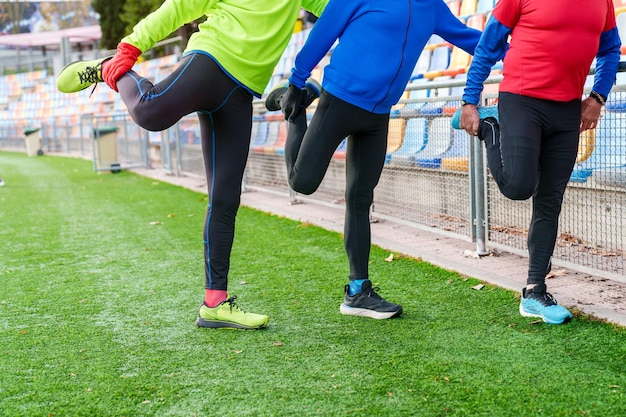 A line of senior male runners stretches legs on a fence at an athletic track preparing for a run