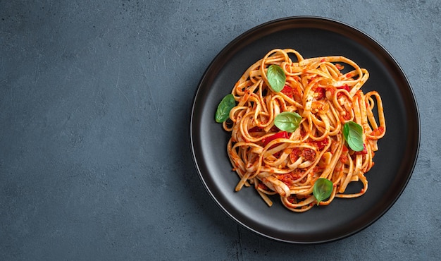 Linguini pasta with tomatoes and basil on a graphite background Italian food