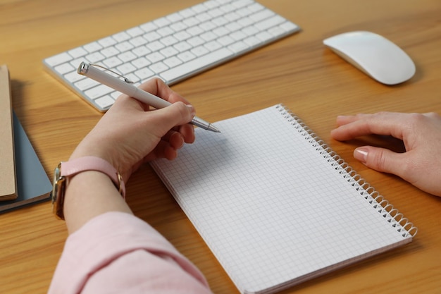 Linkshandige vrouw die in notitieboekje schrijft bij houten bureauclose-up