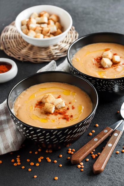 Linzenroomsoep met paprika en crouton in zwarte keramische kommen op donkere achtergrond