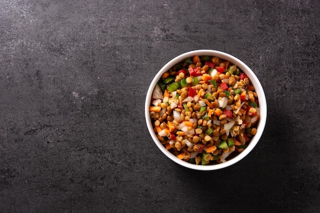 Linzensalade met peppersonion en wortel in een kom op zwarte leiachtergrond